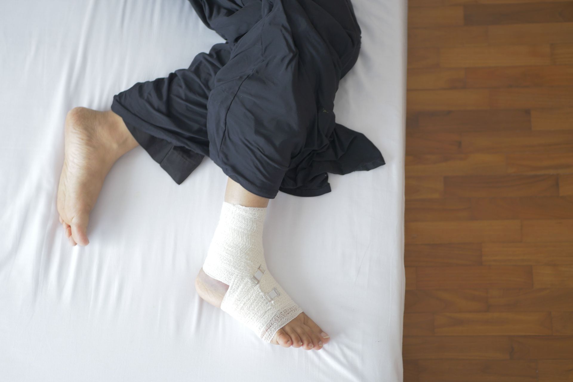 Top view of a bandaged foot resting on a bed, depicting injury and recovery.